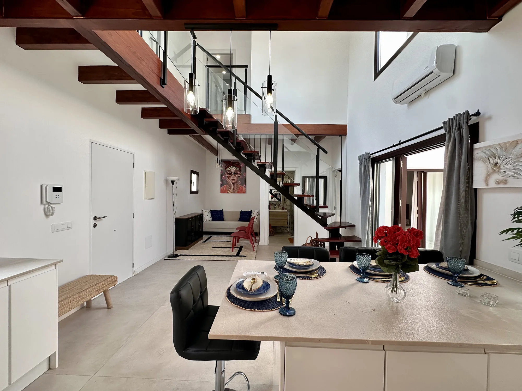 Zona de día con cocina abierta, comedor y escalera de madera y vidrio